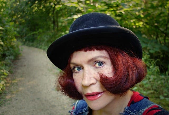 a woman with a red bob hair cut and boller hat taking a selfie in a park