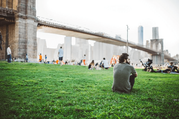 a man sitting on a green lawn below the golden gate bridge thinking of his life purpose.